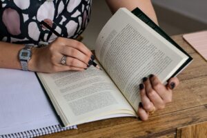 Mulher escrevendo em caderno e lendo livro, representando a transformação da motivação em hábito