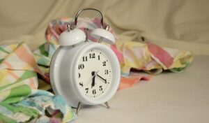 Relógio despertador branco com ponteiros pretos sobre fundo neutro, simbolizando a importância da gestão do tempo convite a autodisciplina.