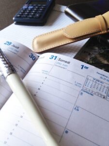 Agenda, calculadora, lápis e ferramentas de organização distribuídos sobre mesa de trabalho. Representando a disciplina para a realização.