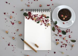 Caderno aberto com caneta ao lado de uma xícara de chá em mesa de madeira clara, criando um ambiente propício à escrita e concentração. Disciplina na rotina e anotar para facilitar.